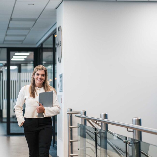 Brandingshoot: Professionele vrouw loopt met laptop door modern kantoor.